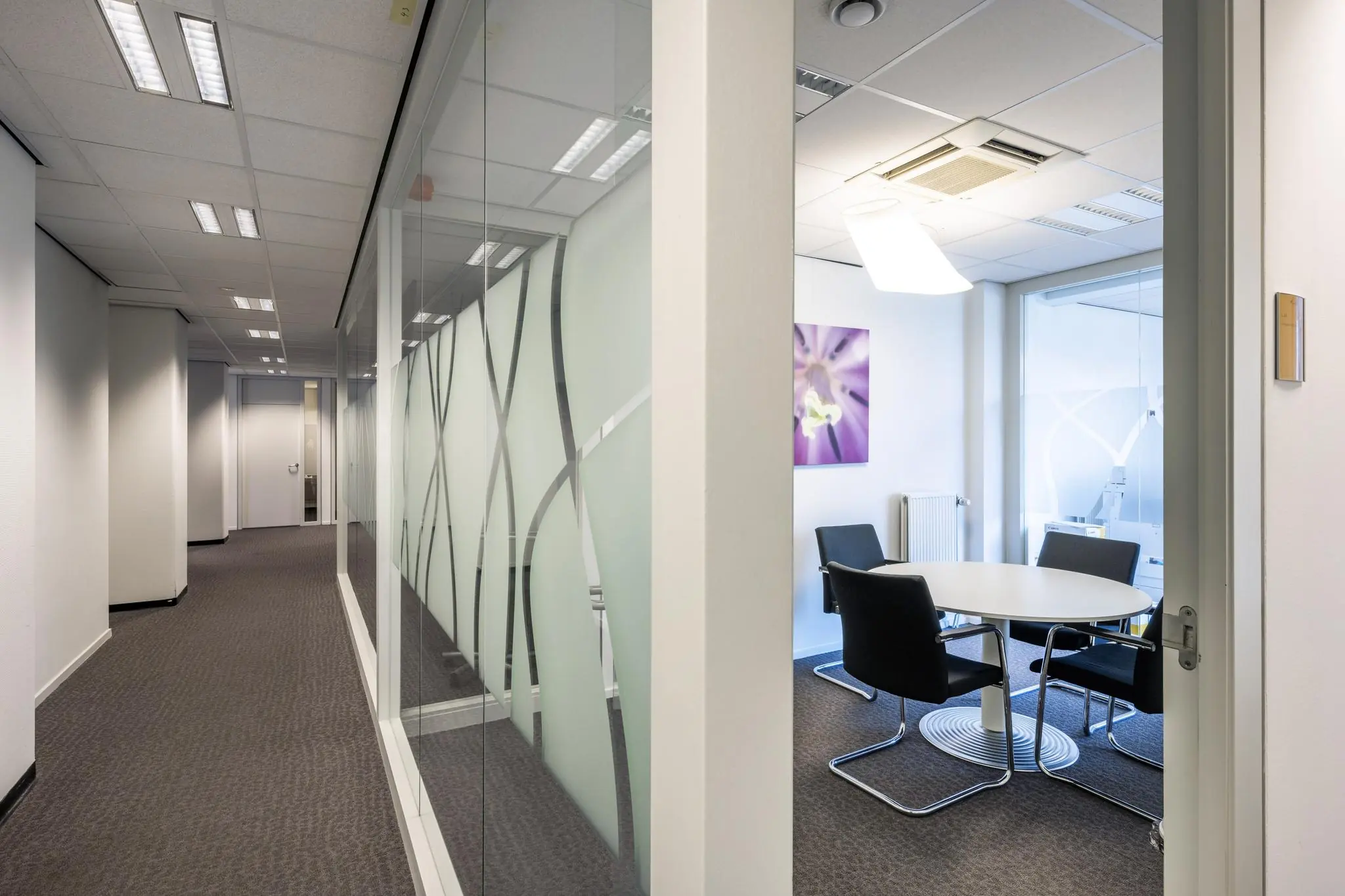 Moderne vergaderruimte aan de Jan Tooropstraat met glazen wanden en vier zwarte stoelen rond een witte tafel.